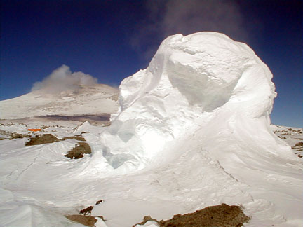 A fumarole ice tower steams in the foreground while Erebus emits a plume in the background.